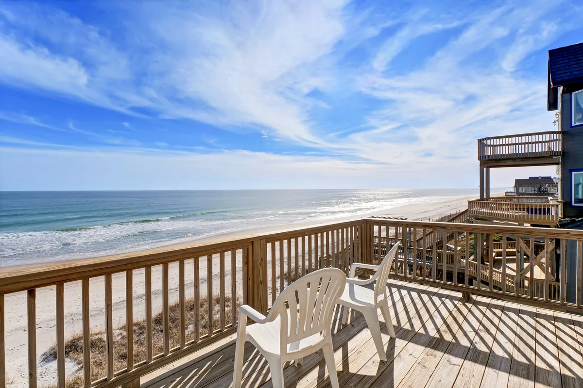 The hero image showcases a spacious oceanfront deck overlooking the pristine sands and rolling waves of North Topsail Beach, with the endless sky stretching above. The inviting outdoor space is perfect for enjoying sunrises, relaxing with a book, gathering for meals, or stargazing at night—all set against a breathtaking coastal backdrop.