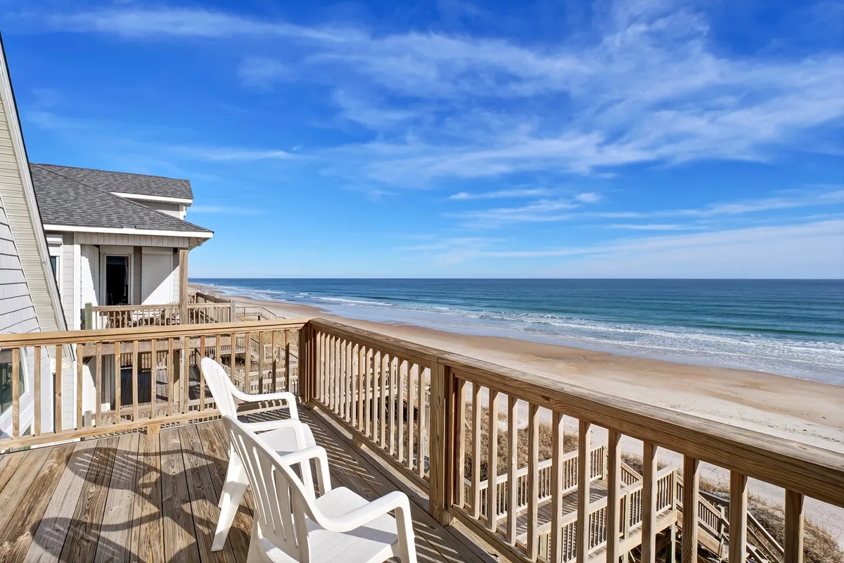 A serene view from a wooden deck featuring white chairs looking out over the ocean. The open sky and calm sea create a peaceful, rejuvenating setting ideal for relaxation, yoga, or simply soaking in the ocean ambiance.