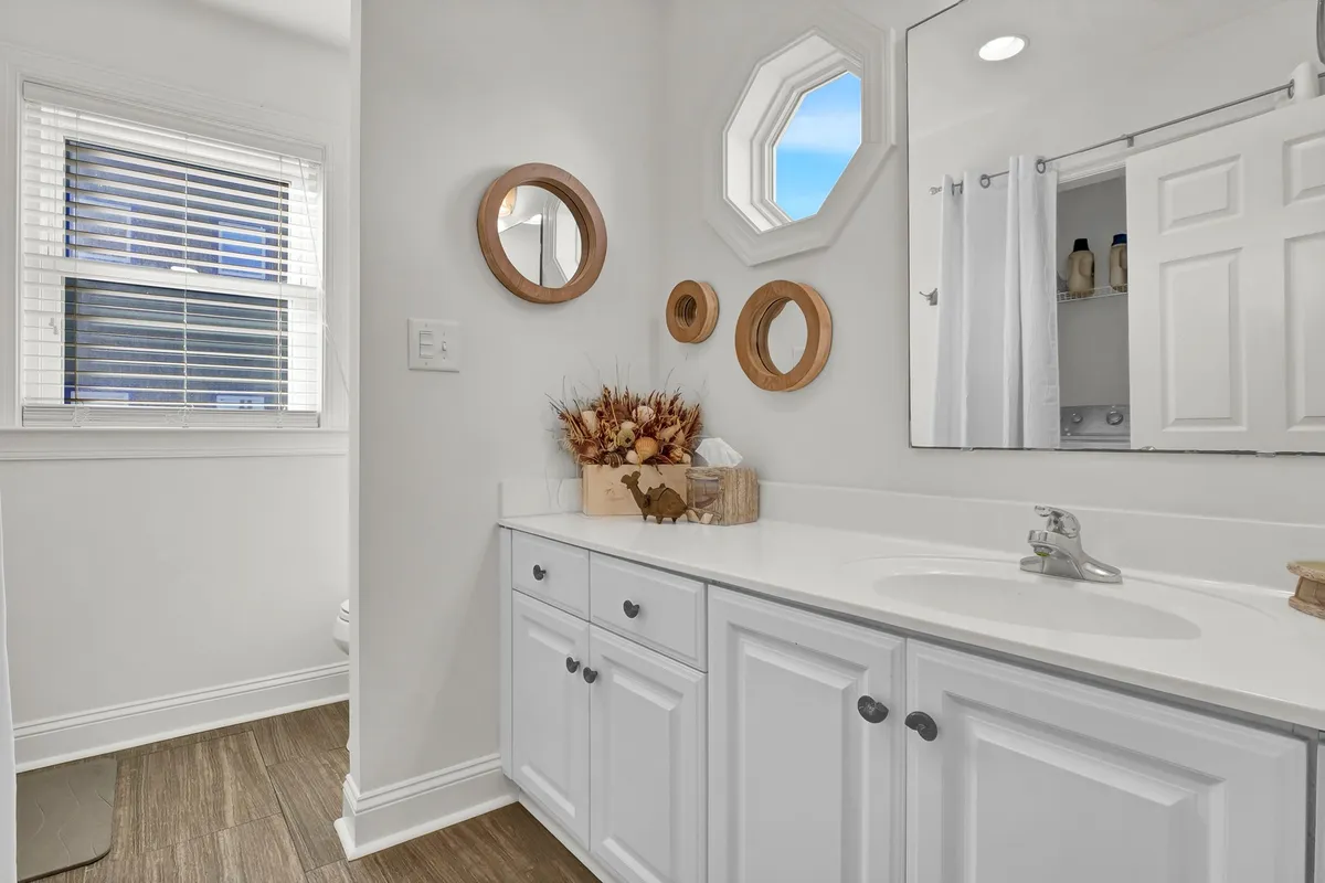 A bright and fresh bathroom vanity with a modern sink, mirrors, and decorative accents like dried flowers, bathed in natural morning light.