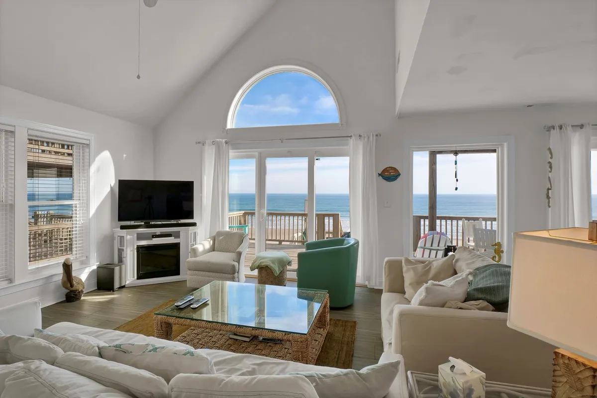 A comfortable, inviting living area with large arched windows framing expansive sea views. Plush seating surrounds a modern TV unit and decorative table, creating a serene space ideal for family conversations, relaxing, or enjoying the ocean backdrop.