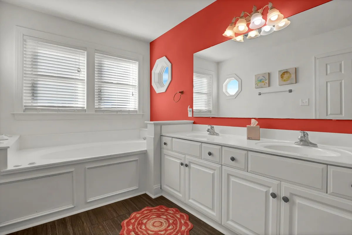 A bright, cheerful bathroom with a double sink vanity, a whirlpool jacuzzi tub, and red accent wall. Octagonal windows allow natural light to illuminate the space, creating a spa-like environment. The fixtures and clean design emphasize comfort and relaxation.