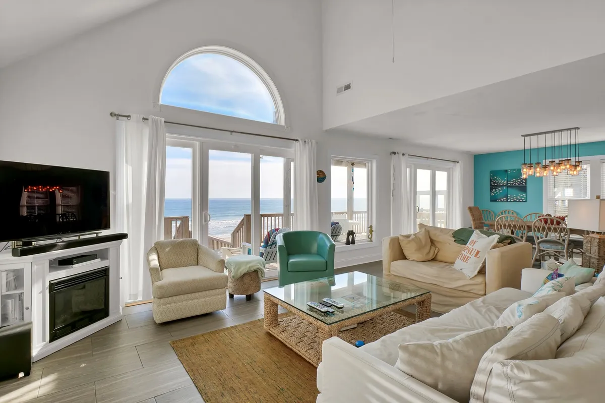 A cozy interior living space with comfortable seating and a coffee table is framed by large windows offering sweeping views of the ocean. The open layout invites family relaxation, morning coffee, or evening gatherings, seamlessly tying the indoors to the shore.